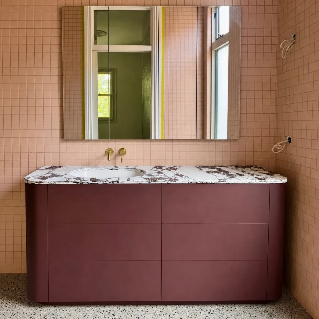 Curved burgundy cabinetry beneath a white patterned surface and mirrored cabinets