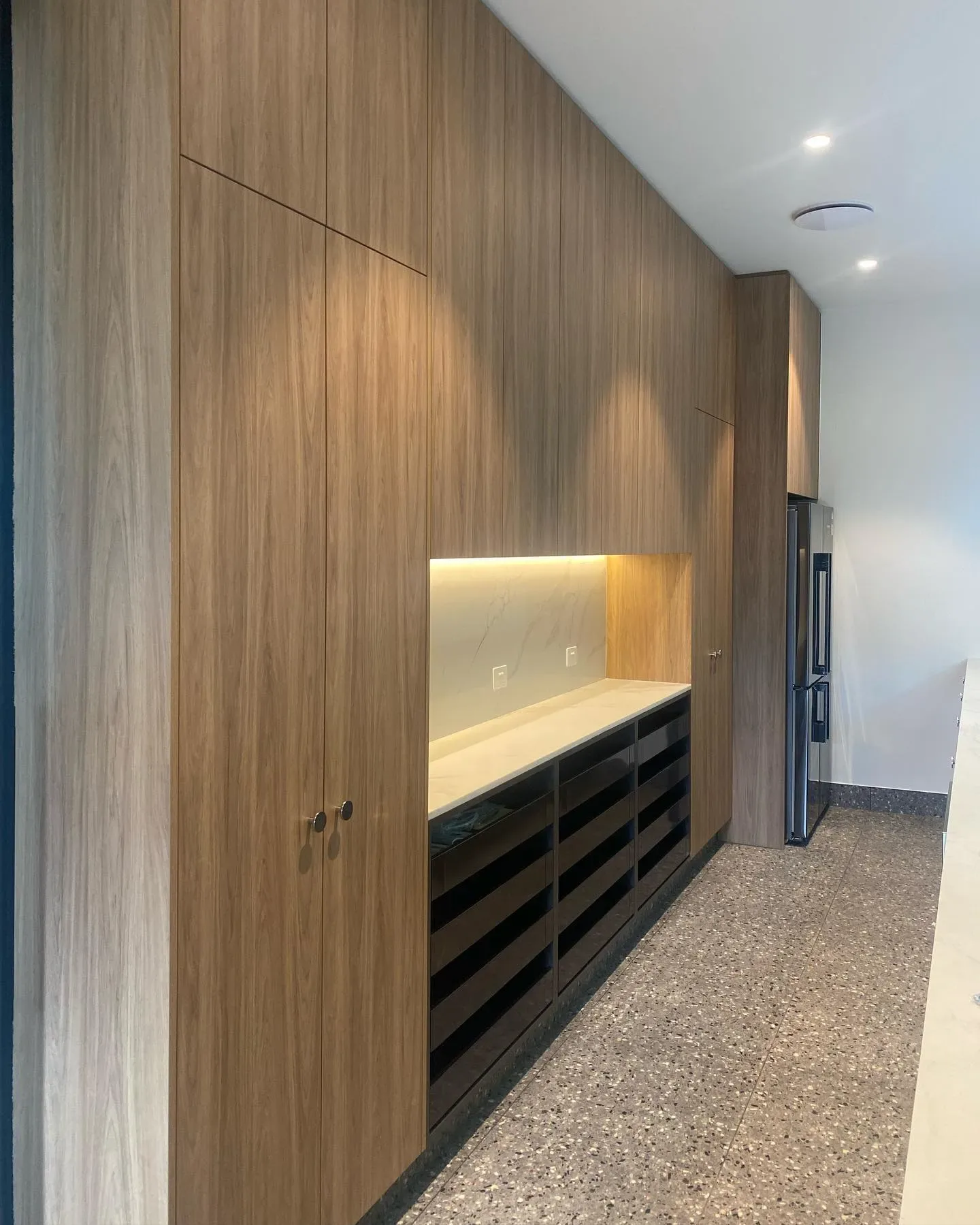 Tall wood-grained cabinetry with an illuminated recessed work surface and dark drawers