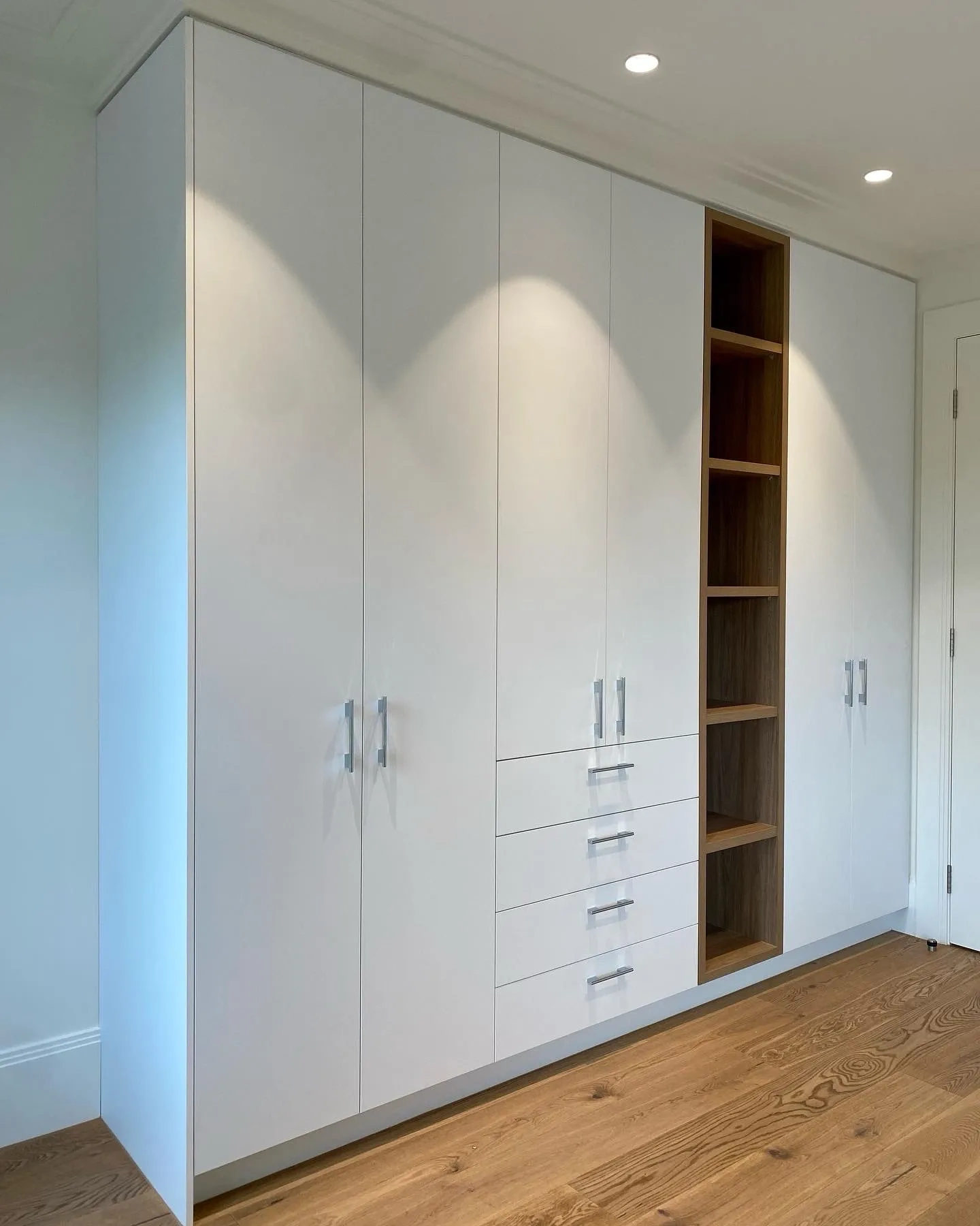 Tall white built-in cabinetry with drawers and open wood-grained shelving