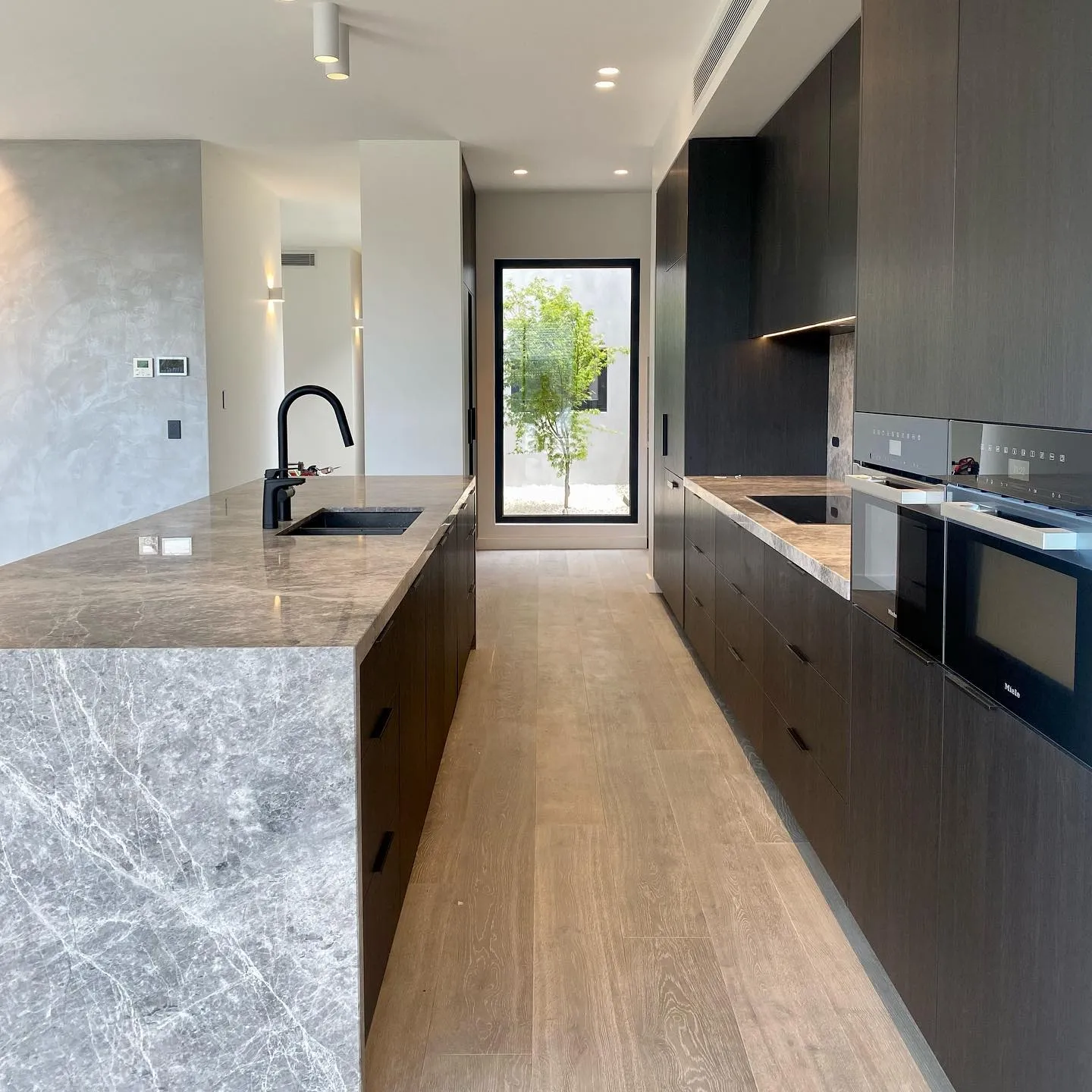 Dark timber galley kitchen with natural marble island and integrated Miele appliances