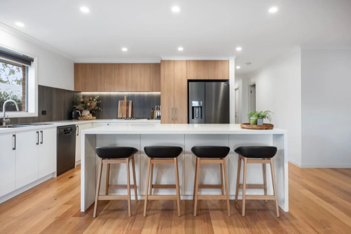 Pale cabinets, a long white island and four dark stools